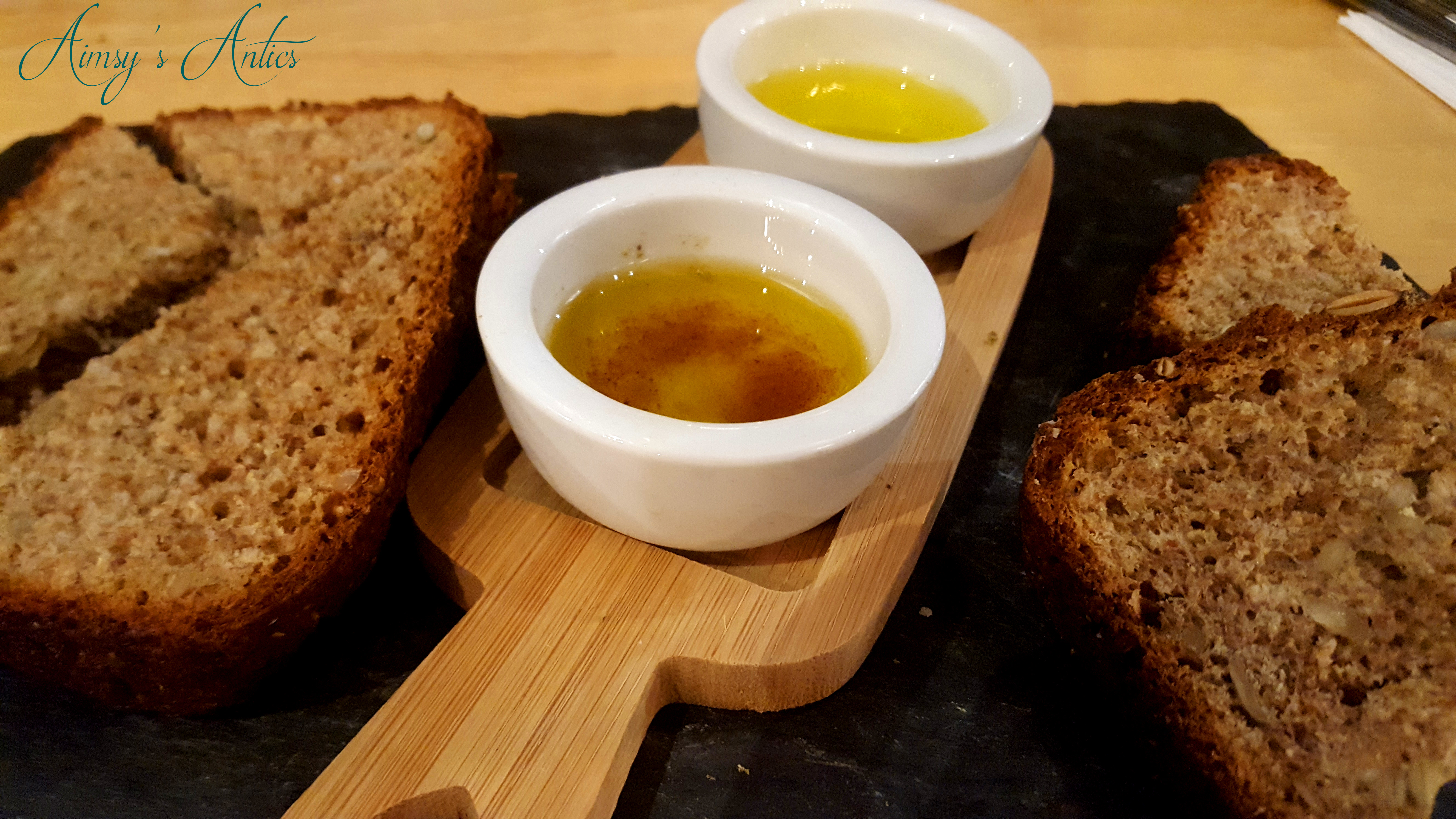 Image of several slices of homemade wholemeal bread with two pots of oil in the middle. One oil infused with orange, and the other with chilli. All on a slate plate.