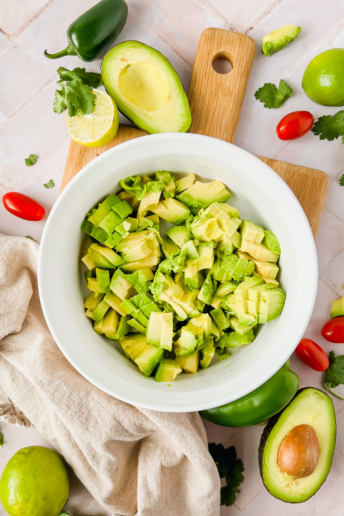 chopped avocado in white bowl on wood cutting board with avocado crack dip ingredients surrounding.