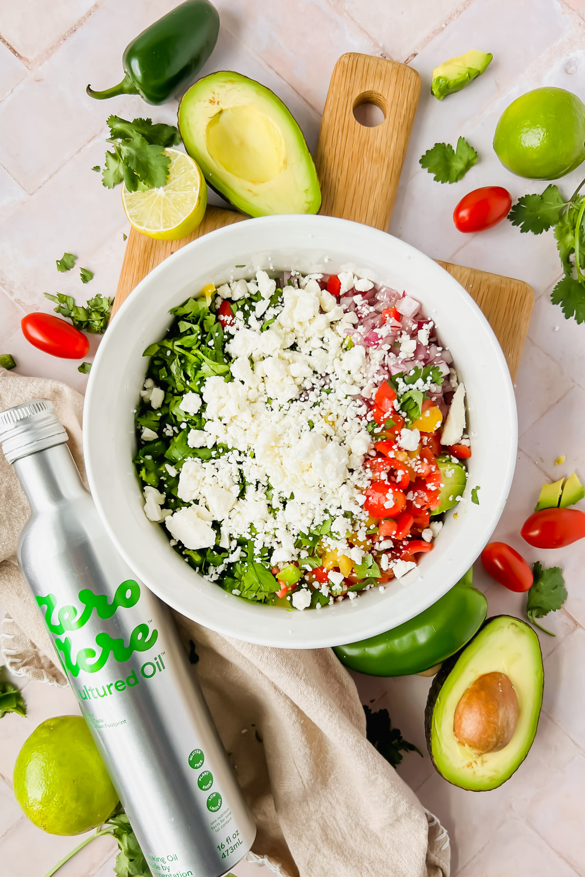 ingredients for avocado crack dip chopped and placed in white bowl before tossing with zero acre cultured oil bottle beside bowl.