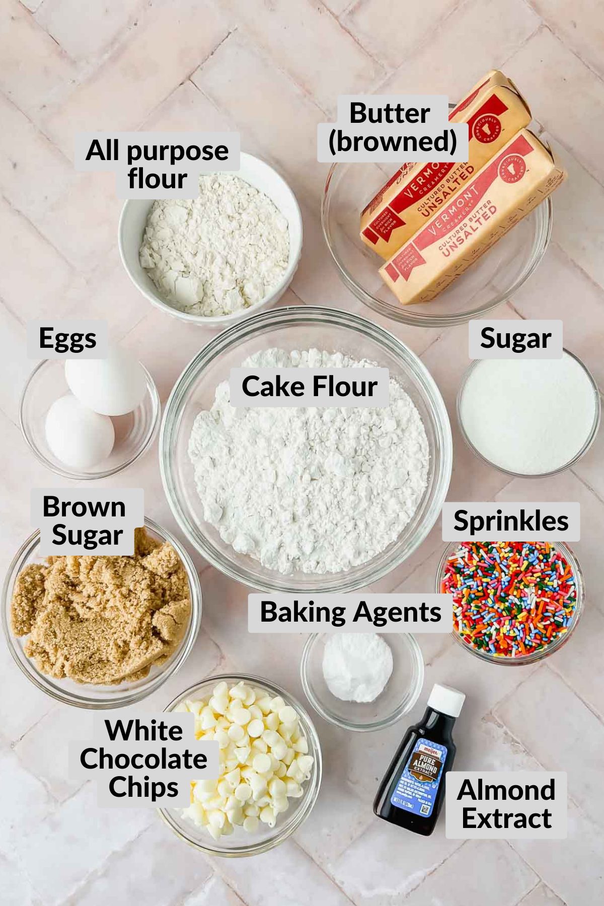 ingredients for funfetti chip cookies in individual bowls on pink tiled background. 