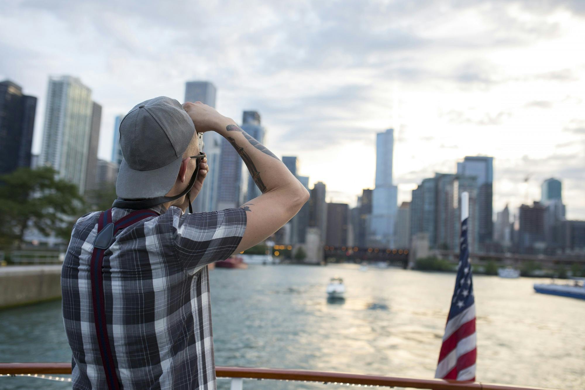A person on a boat photographs a cityscape with tall buildings; an American flag is on the boat's stern.