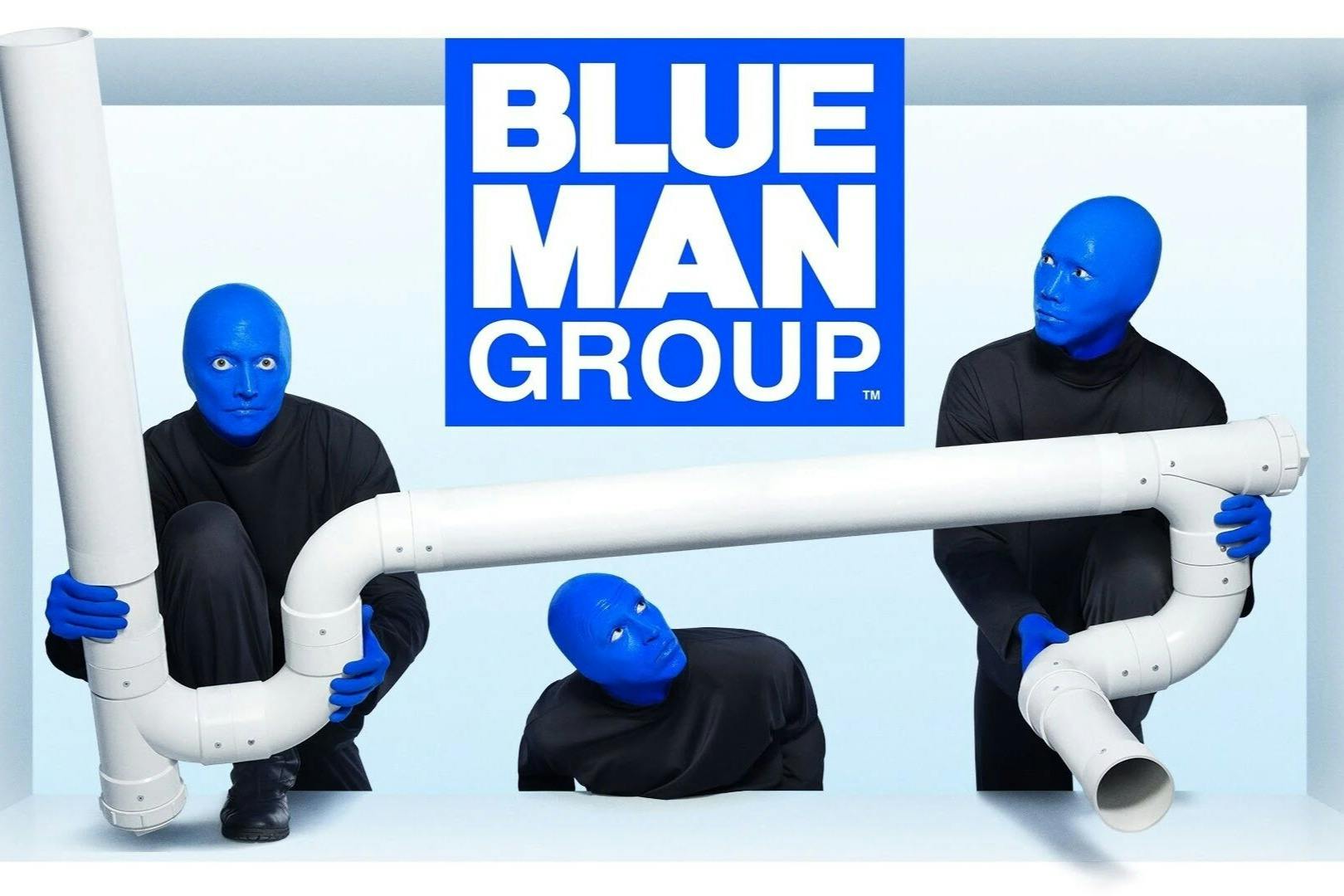 Two individuals with blue-painted faces and black clothing interact with white PVC pipes. 