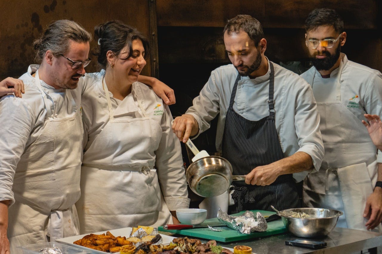 Chefs in white uniforms and aprons prepare and plate food in a professional kitchen.
