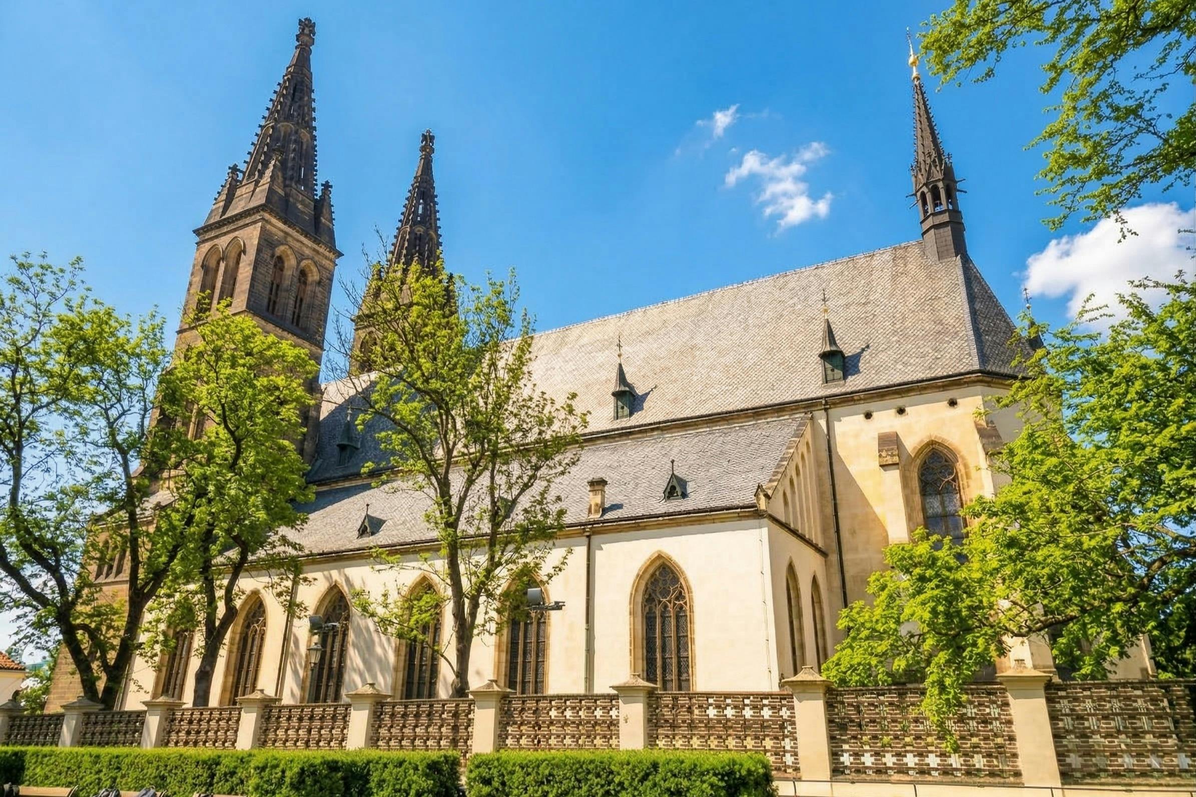A historic church with pointed spires, arched windows, and a stone facade, surrounded by trees under a blue sky.