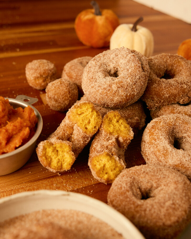 pumpkin donuts on a table, one split open to see orange donut inside