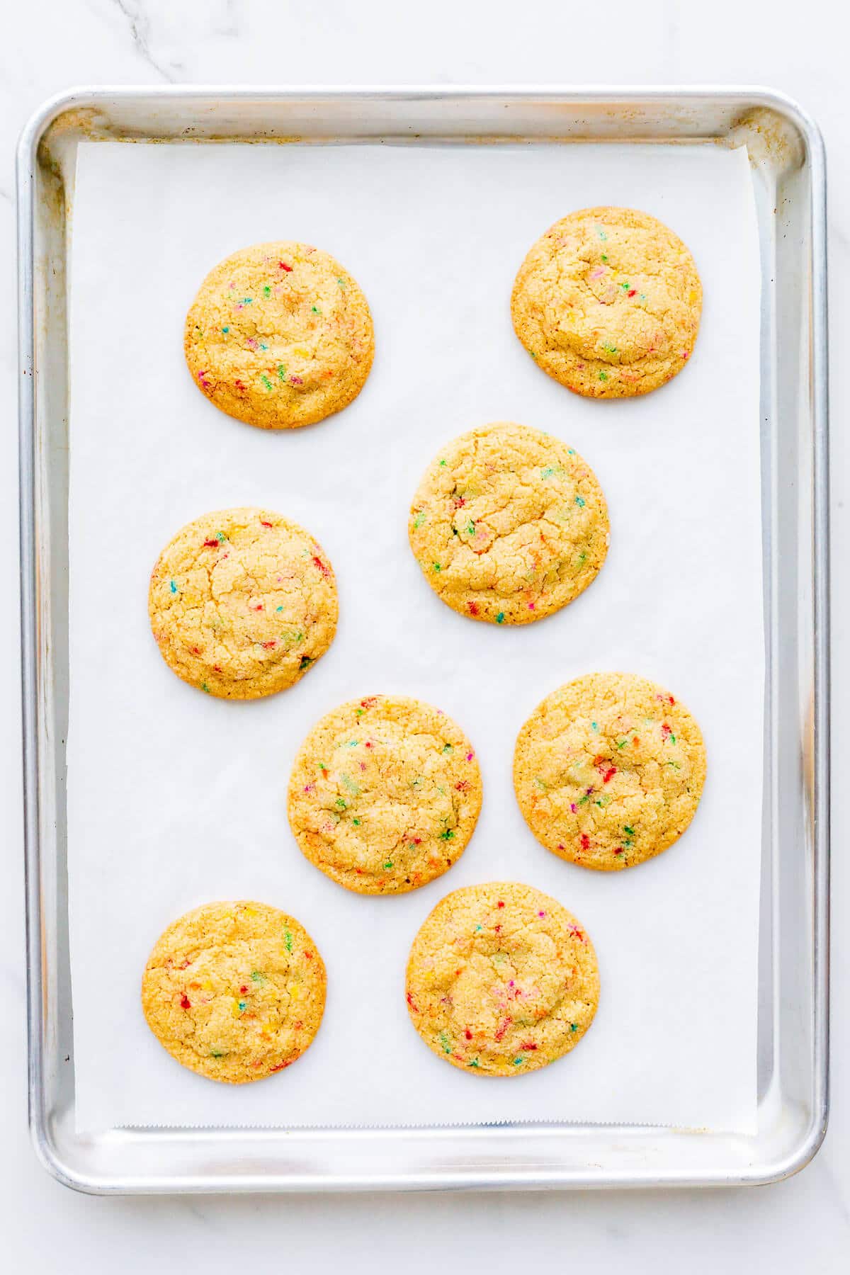 A sheet pan of freshly baked sugar cookies with sprinkles.