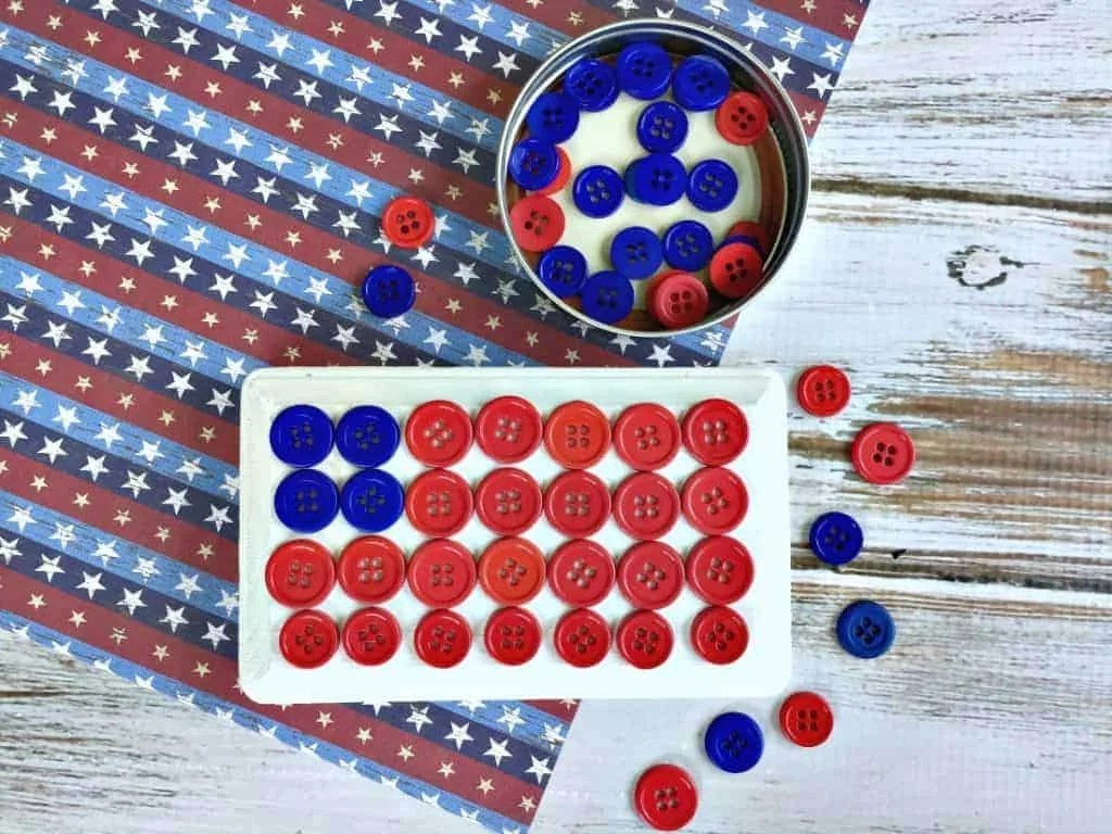 A white plaque with red and blue buttons glued to it to make an American flag. 
