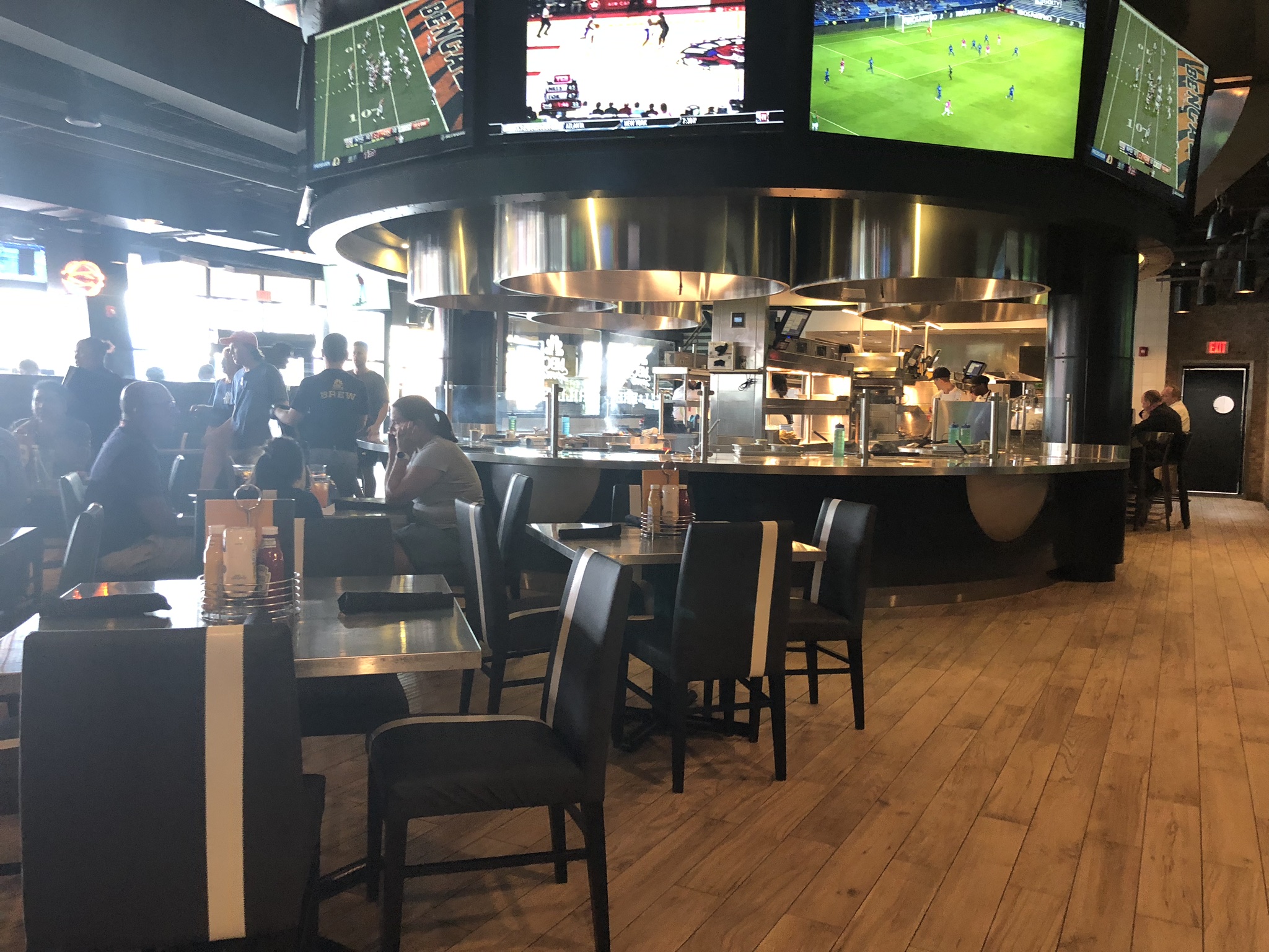 inside restuarant featuring cooking area and normal chairs, plus tvs mounted high