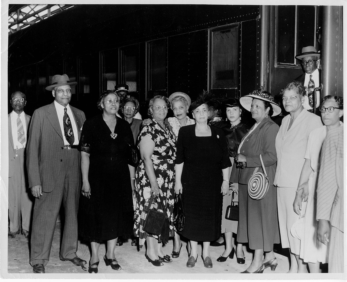 Group photograph of church members standing beside a train Black