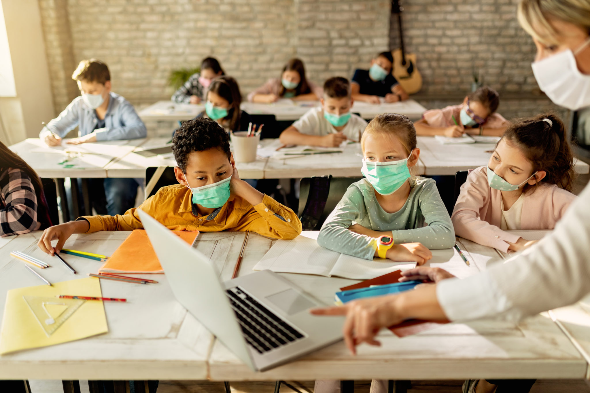 Elementary students wearing face masks while using laptop with their
