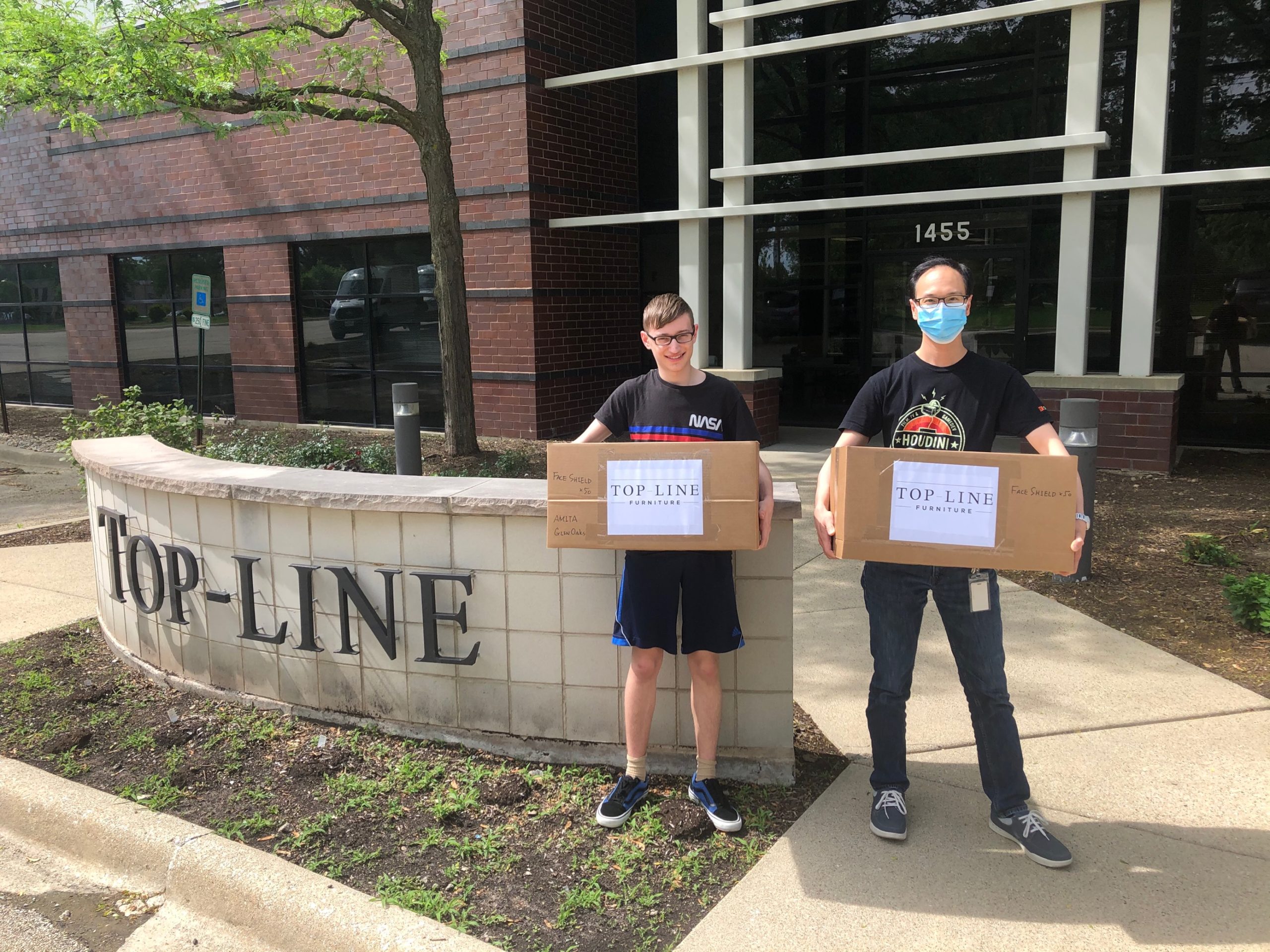 Inspire Q team member Allen Yau stands with a volunteer from GetUsPPE.org. Both are holding packages of face shields for essential workers. 