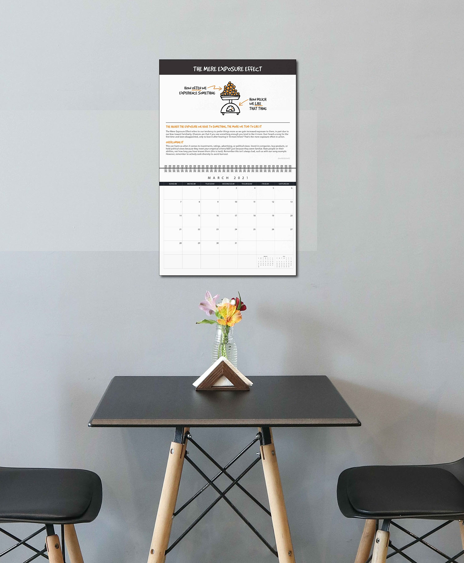Calendar hanging on a simple wall above a table with two chairs and a vase of flowers 
