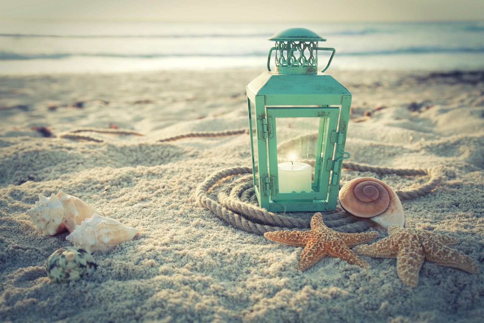 Crossprocessed lantern on beach with shells and rope at sunrise The
