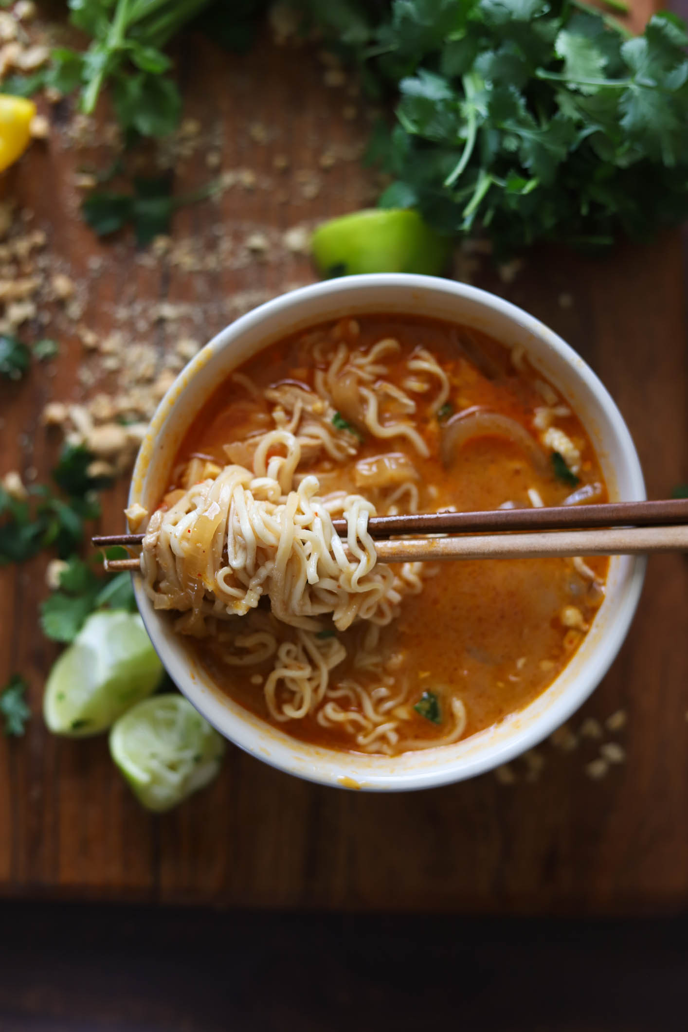 overhead shot of Thai Peanut Curry Ramen Noodle Bowls with fresh lime and cilantro on a cutting board 