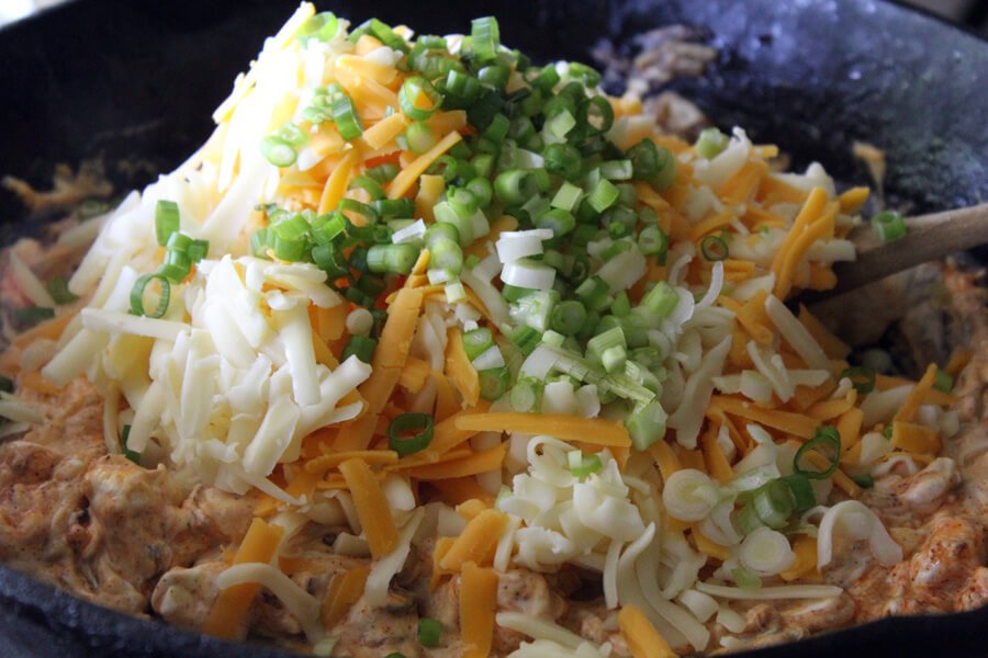 In the SEC, it is always Go Big Or Go Home, so don't skimp on the cheese! two types of shredded cheese and green onions being stirred into hot ham dip