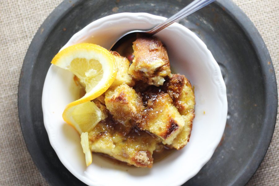 Loving our Orange + Spiced Rum Bread Pudding, extra rum sauce for me, please. A bowl of warm bread pudding on a metal charger plate, topped with a slice of fresh orange and rum sauce