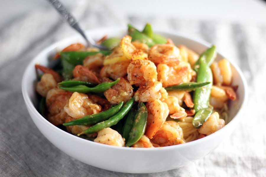 Serve your Lemon Garlic Shrimp with angel hair pasta or rice for a tasty meal. A white bowl full of prepared lemon garlic shrimp on a bed of snow peas and angel hair pasta