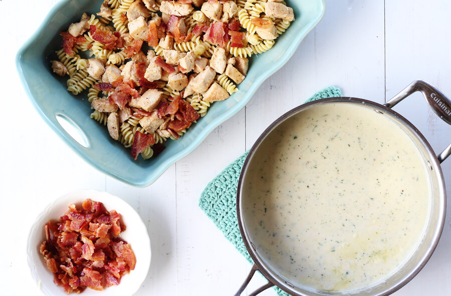 Overhead shot of ingredients for Chicken Bacon Ranch Casserole including a sauce pan of homemade ranch white sauce.