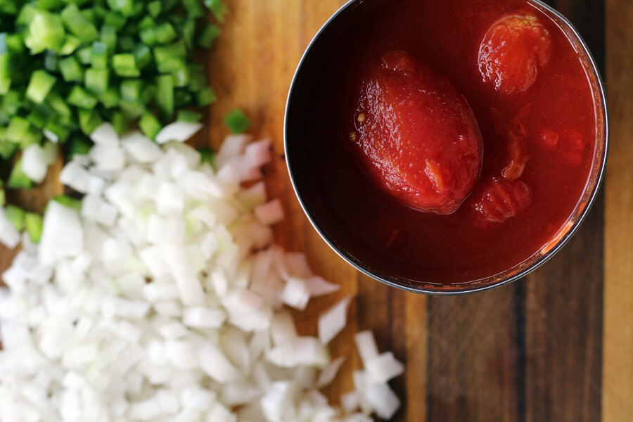 An overhead shot of a can of whole, stewed San Marzano tomatoes next to diced bell peppers and onions