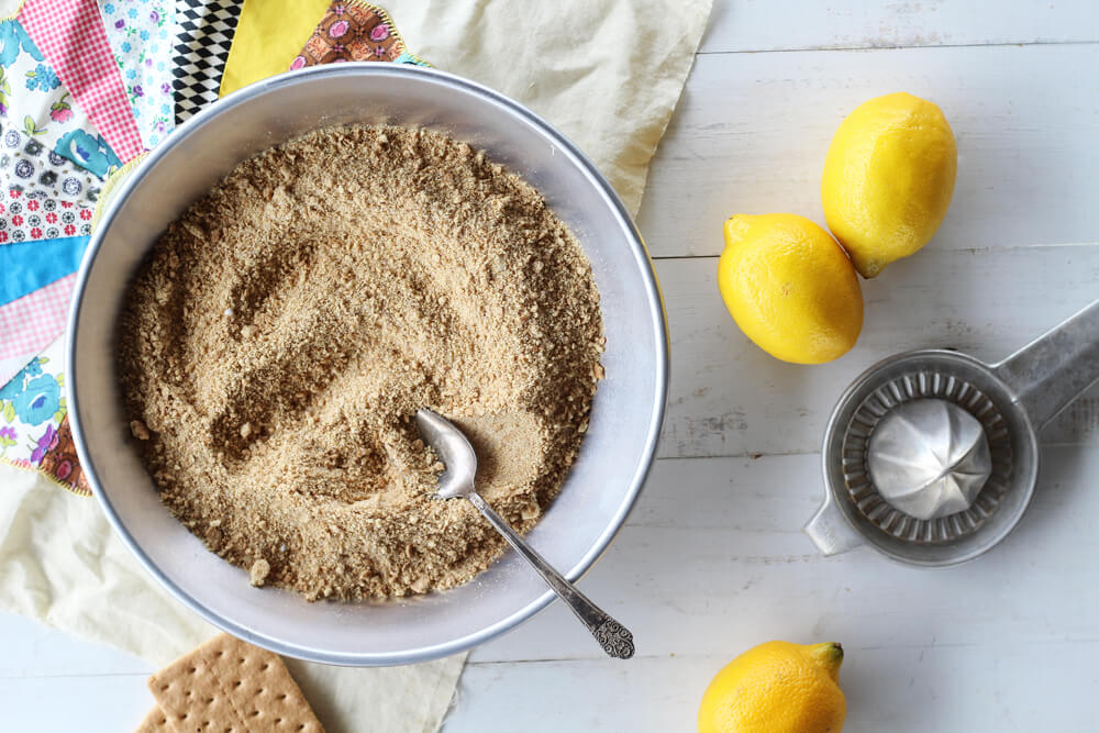 graham cracker crumbs in a metal pie next to fresh lemons