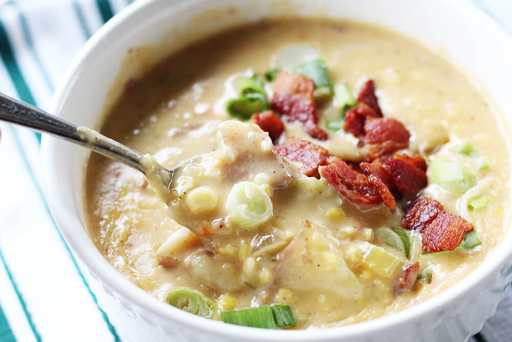a white bowl with chowder topped with green onions and bacon