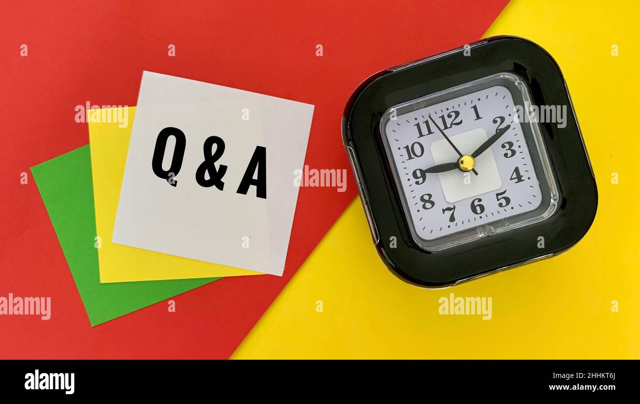 Questions and Answers message on white notepad. With alarm clock, red
