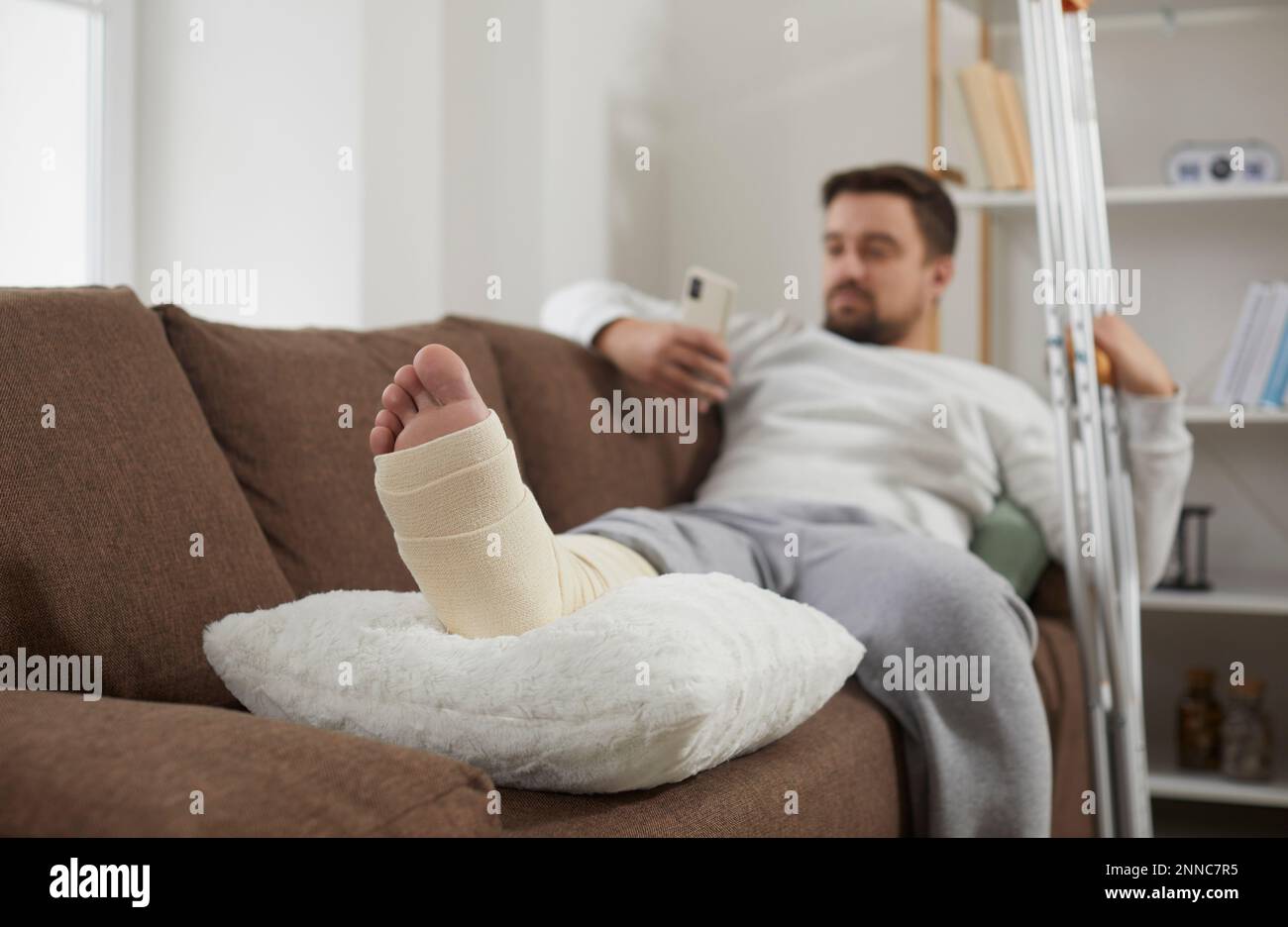 Man with an injured, broken leg relaxing on the sofa, with his foot resting on a cushion Stock