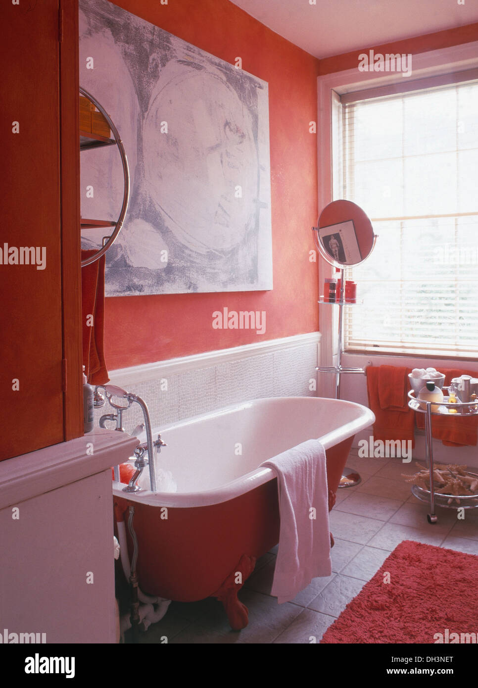 Roll top bath below large abstract painting in red bathroom with