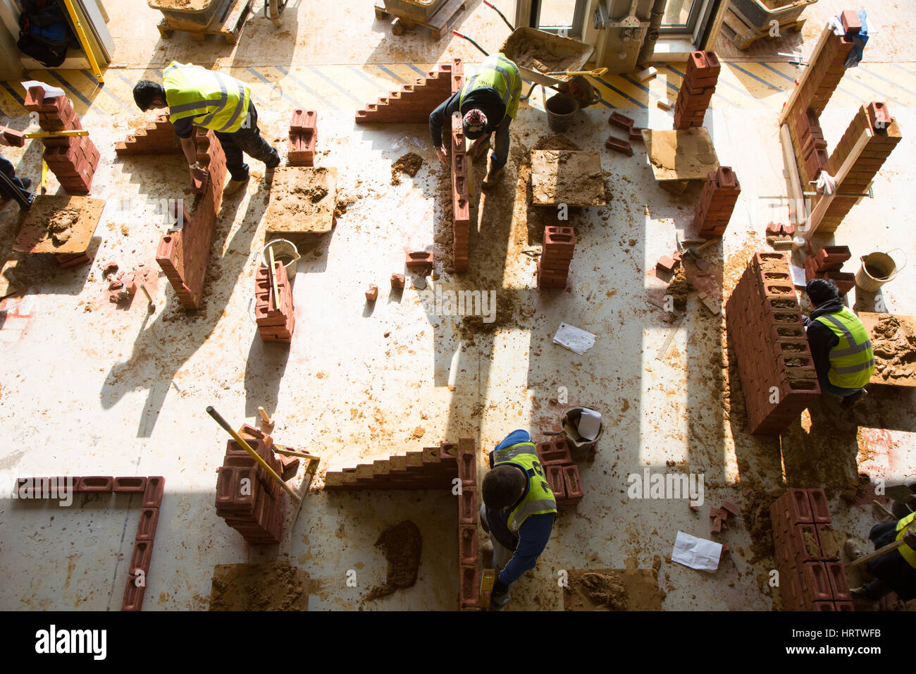 Apprentice builders learn how to construct a wall using bricks and