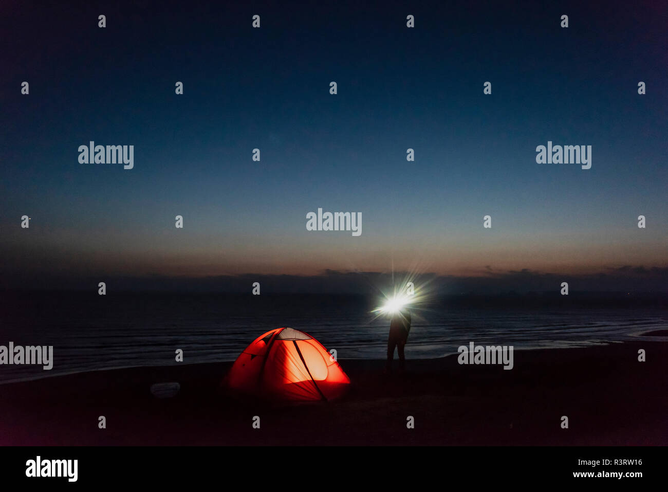 Young man camping on the beach, using flashlight Stock Photo Alamy