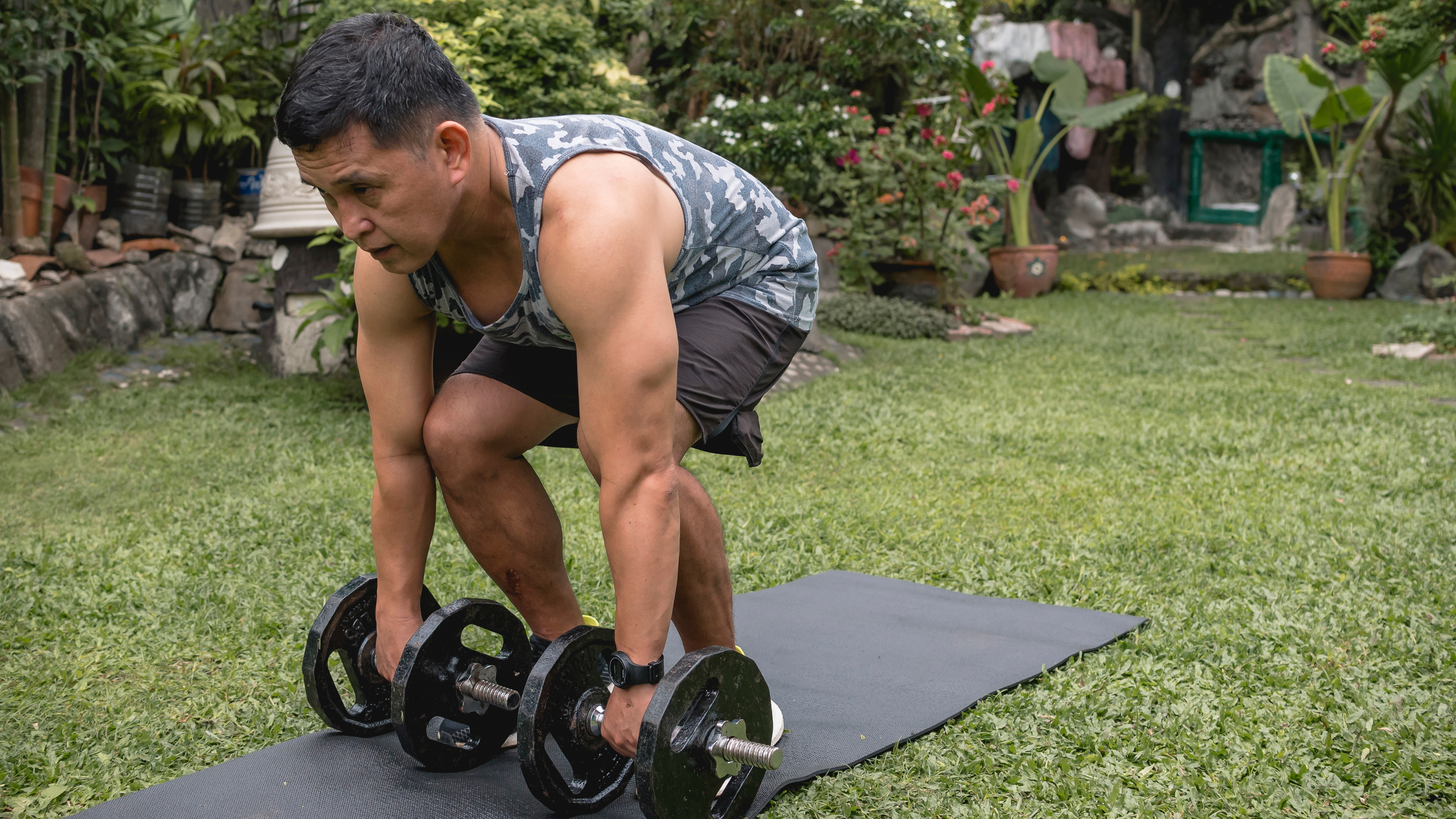 Man doing dumbbell deadlifts in grassy yard