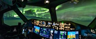 La vista desde el interior de la cabina muestra los controles de un avión y una fuerte aurora con cintas de luz brillantes hasta donde alcanza la vista.