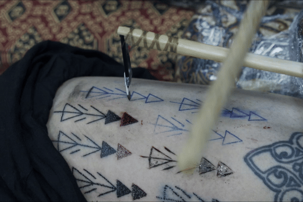 Danny Riday&rsquo;s leg being tattooed by another tattoo artist using boar tusk comb; this is the technique traditionally used in Austronesia.