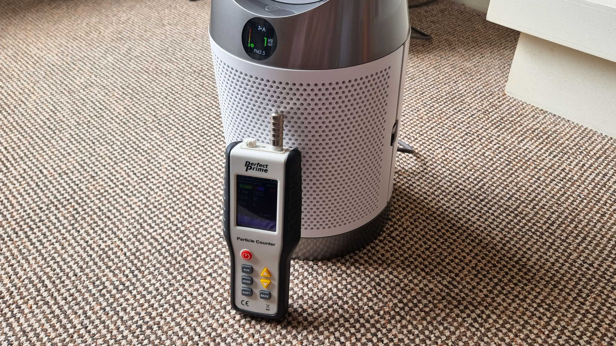 An air particle monitor standing next to the Dyson Purifier Cool PC1