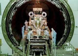 Técnicos vestidos con trajes limpios atienden una gran pieza de maquinaria en una puerta circular que se extiende por varios metros.