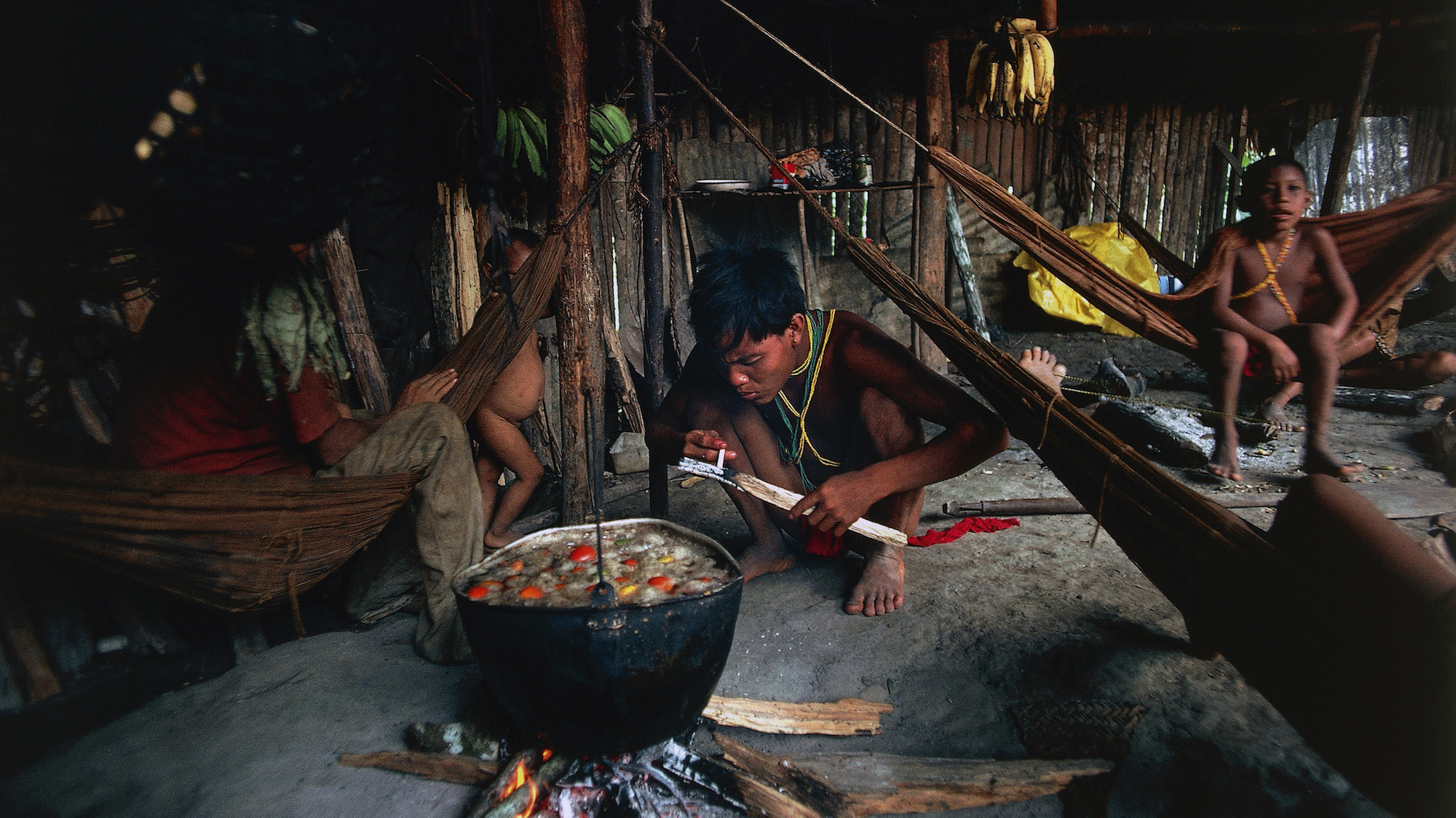 Yanomami men and children cook together in a hut in the Amazon rainforest.