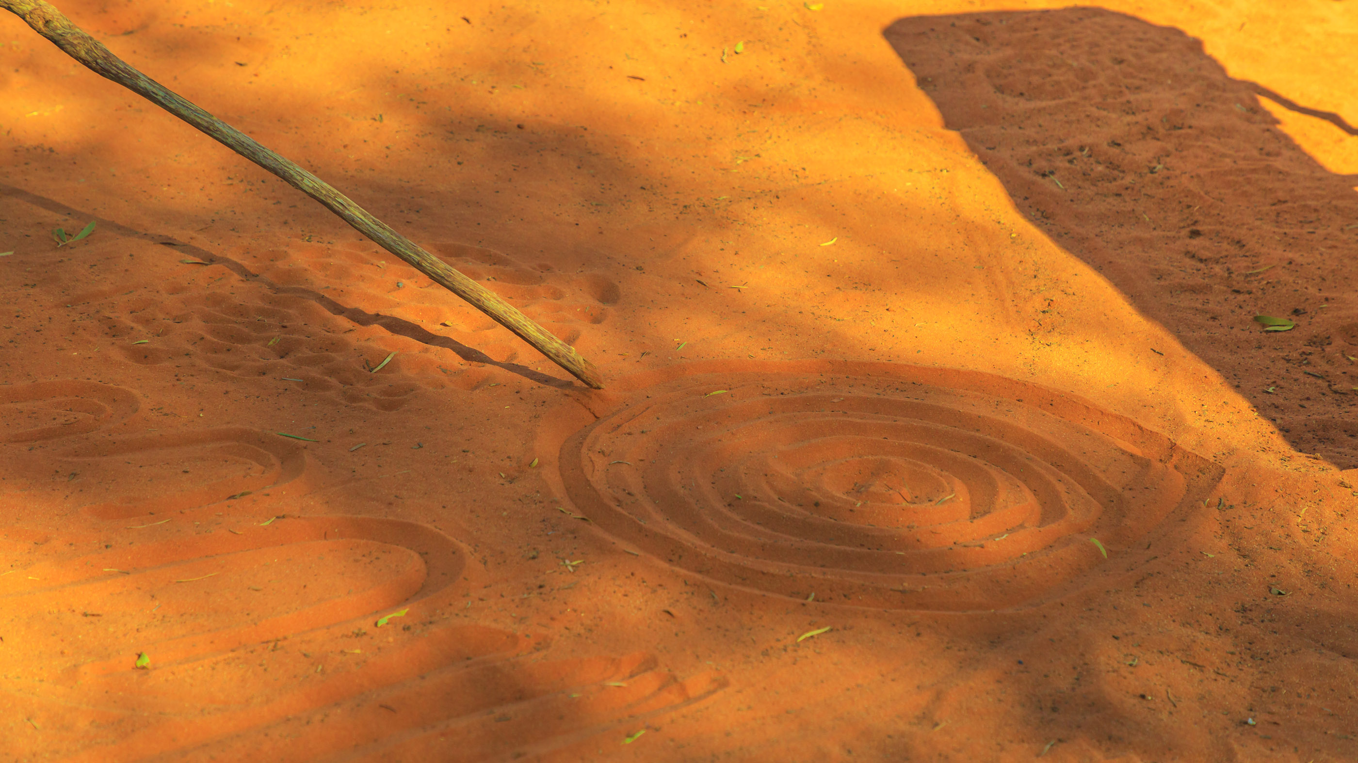 Aboriginal people creating shapes with red sand on the ground in Aboriginal art style.