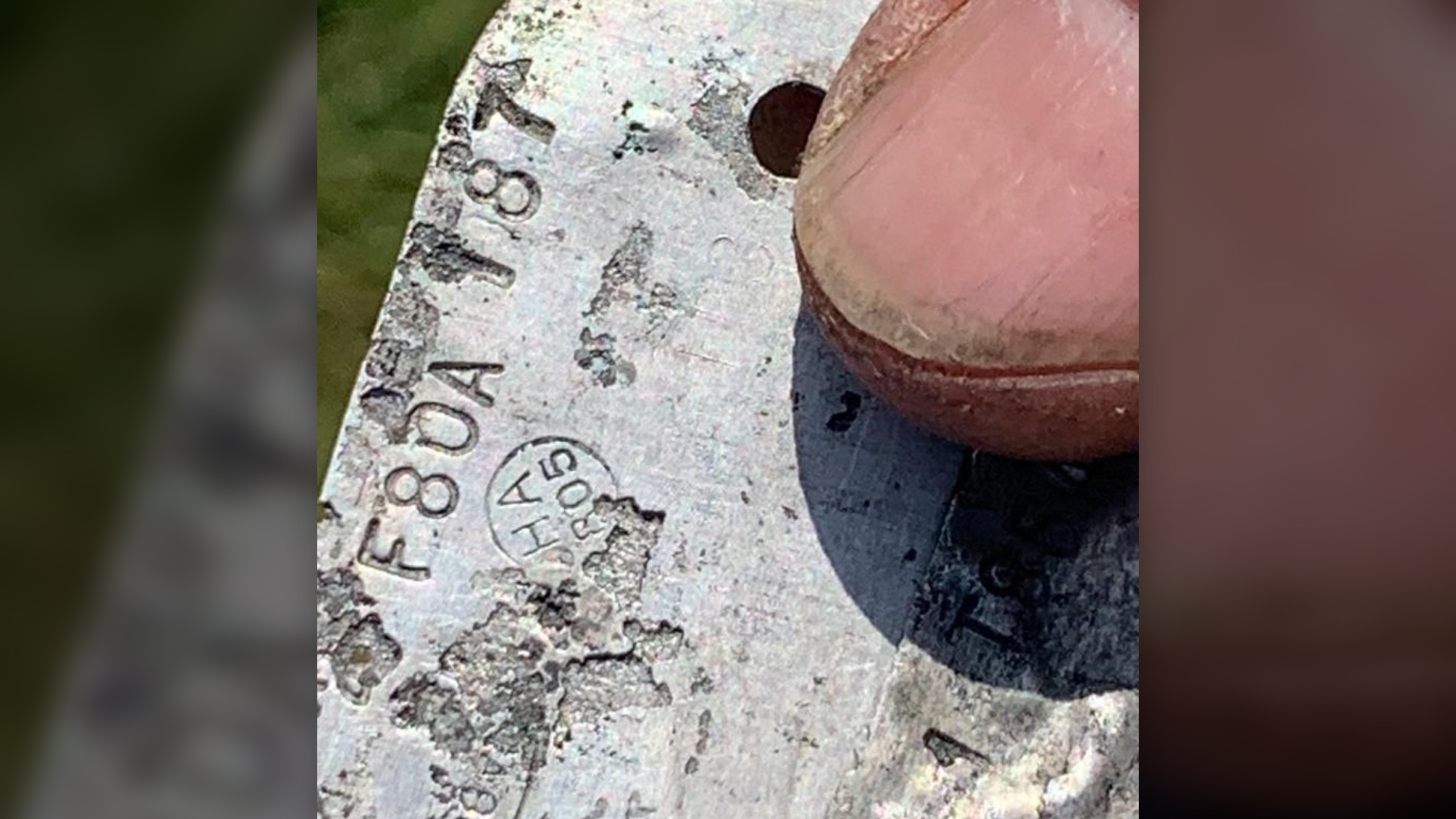 We see a person&rsquo;s thumb over a metal piece that has imprinted numbers and letters.