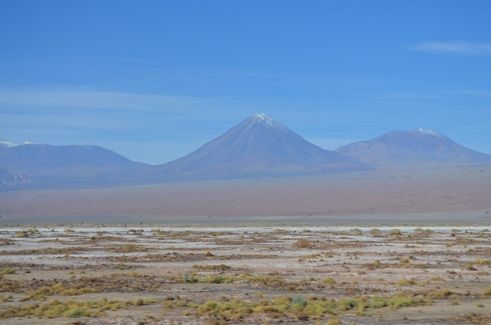 Green scrub dots the ground in some places in Chile&rsquo;s Atacama desert, while pointed volcanoes tower over the scene.