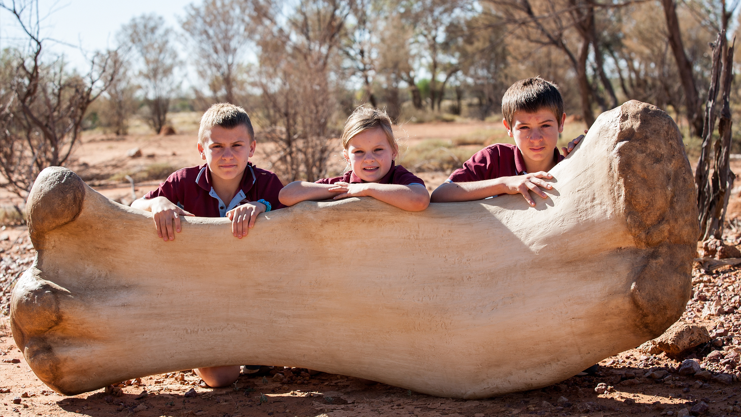 Students from Eromanga State School size up against a replica of Cooper&rsquo;s femur (thigh bone) at the Eromanga Natural History Museum.