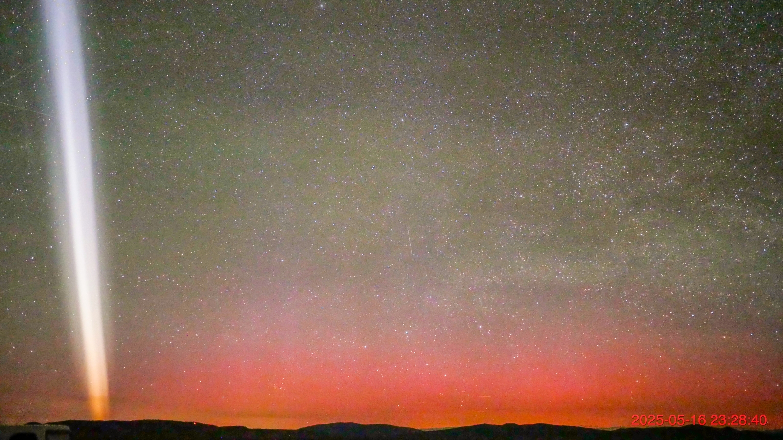 A white streak of light in the night sky with red auroras just above the horizon