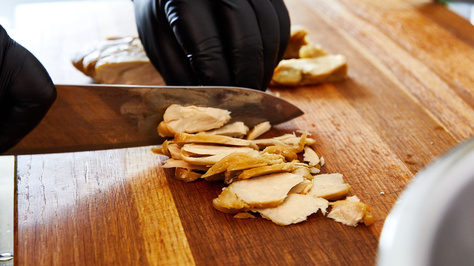 close up of a person�s gloved hands as they slice through a lab-grown chicken breast with a knife on a cutting board