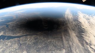 La sombra de la luna aparece como una mancha negra sobre partes nevadas de Canadá y Maine desde la estación espacial, con algunos equipos de la estación a la vista.