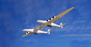 Un avión blanco de doble fuselaje con un avión de cohete experimental debajo de su ala