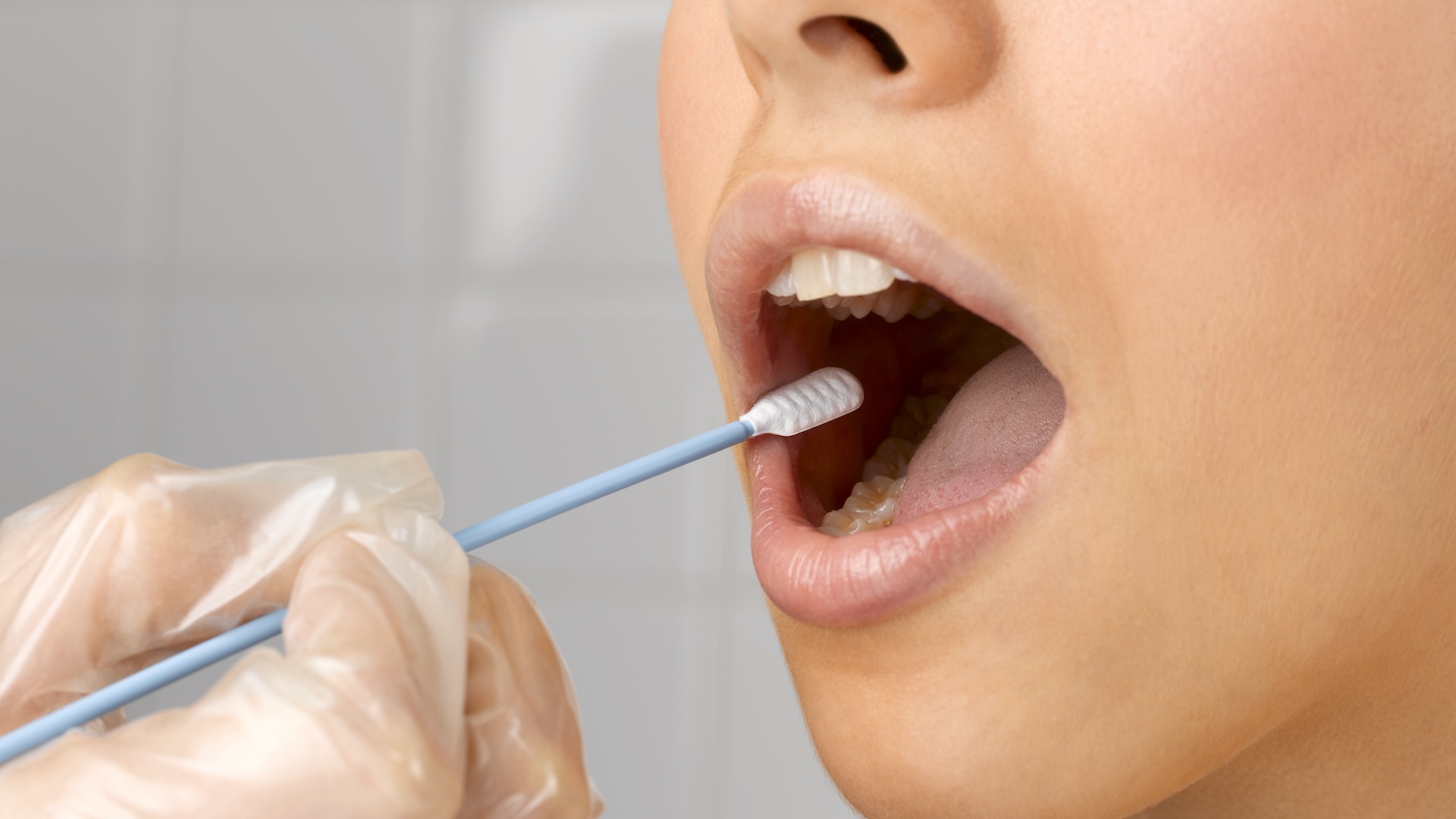 A doctor wearing clear gloves swabs the inside of a woman�s cheek with a long q-tip