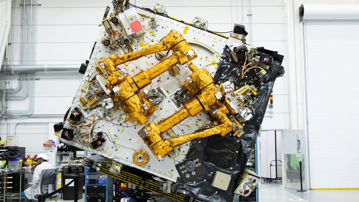 Un satélite en forma de cubo con dos brazos multiarticulados dentro de una sala limpia.