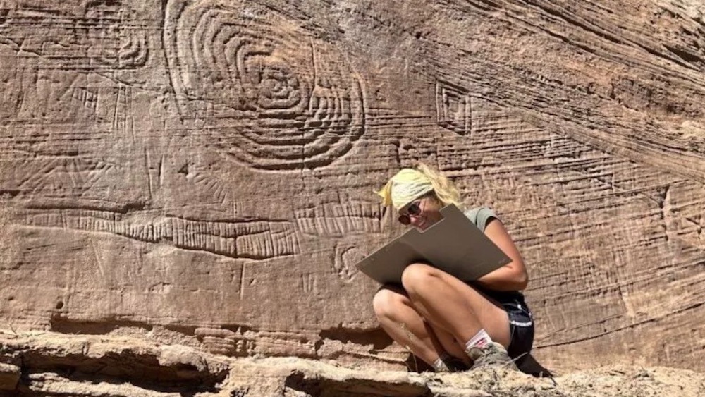 A woman crouches next to petroglyphs.