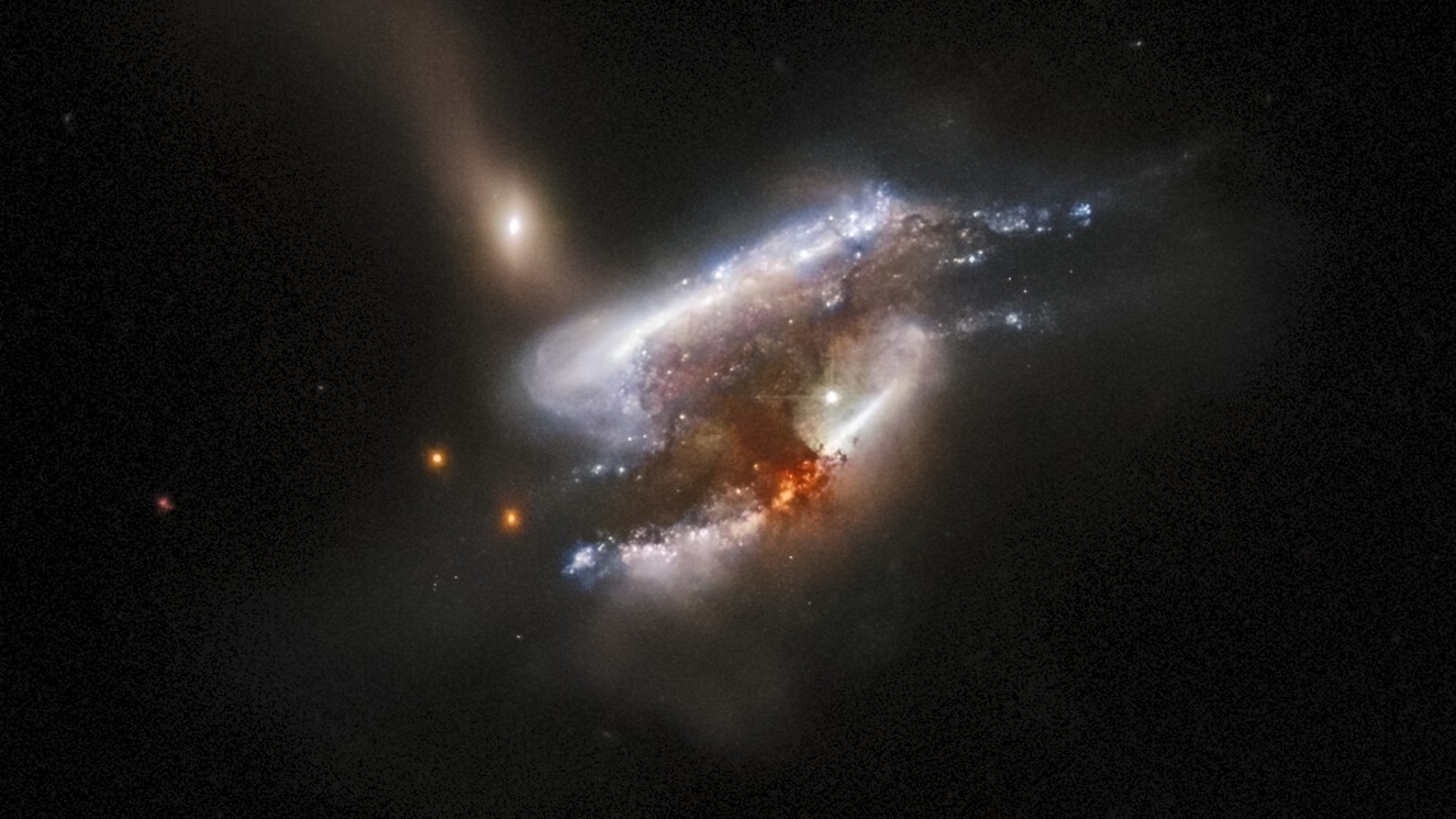 A telescope image of three galaxies swirling around one another as they collide, with a bright orange burst of radiation at the center