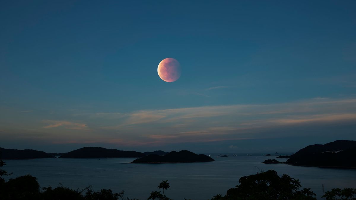 Eclipse lunar en un cielo azul sobre un cuerpo de agua.