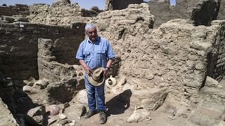 Un hombre con una camisa azul se encuentra junto a las ruinas de ladrillo de una ciudad antigua